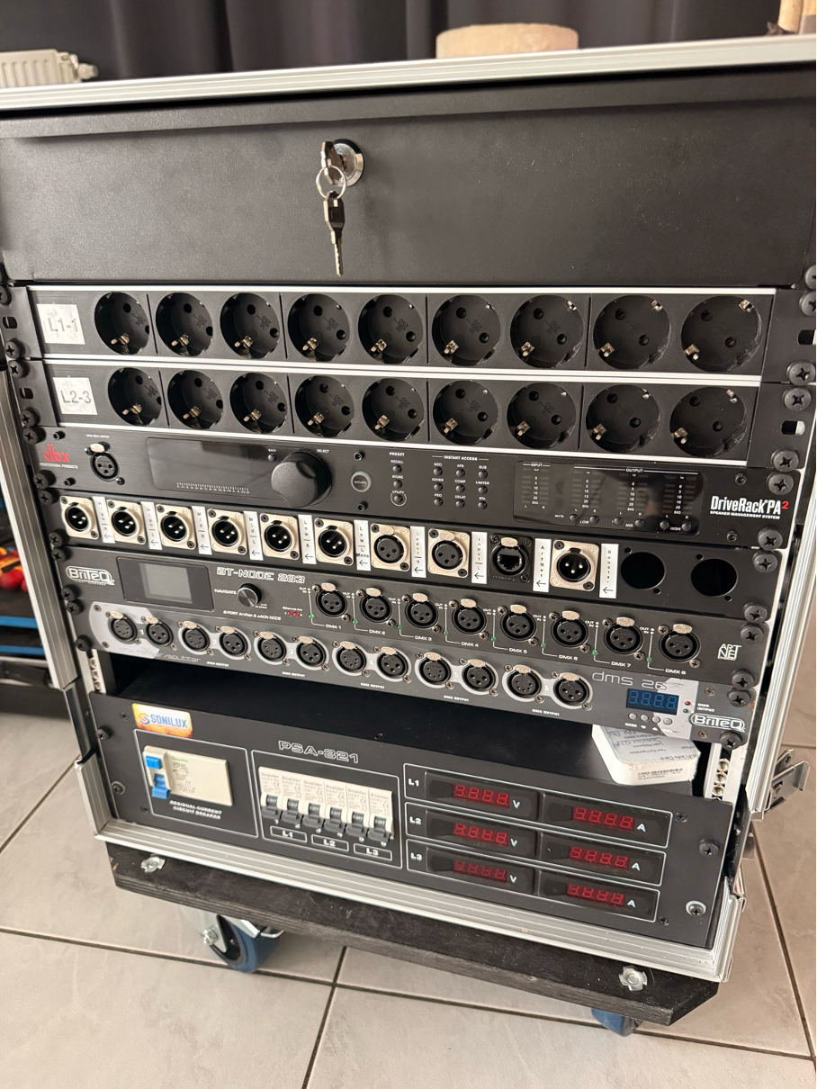 Rij aansluitpanelen en rackapparatuur met meerdere XLR- en stroompoorten, display en kabels in een flightcase. Artnet - DMX Booster en Audioprocessing